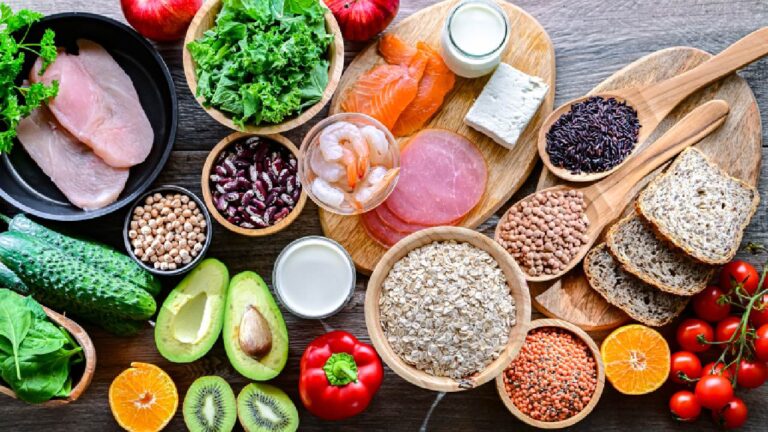 A variety of fresh anti-inflammatory diet foods including leafy greens, salmon, whole grains, legumes, avocado, berries, and nuts displayed on a wooden table.