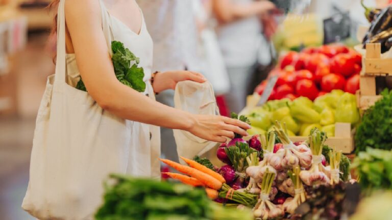 A woman shopping for fresh vegetables at a local market, placing produce into a reusable bag — a practical example of healthy eating on a budget.