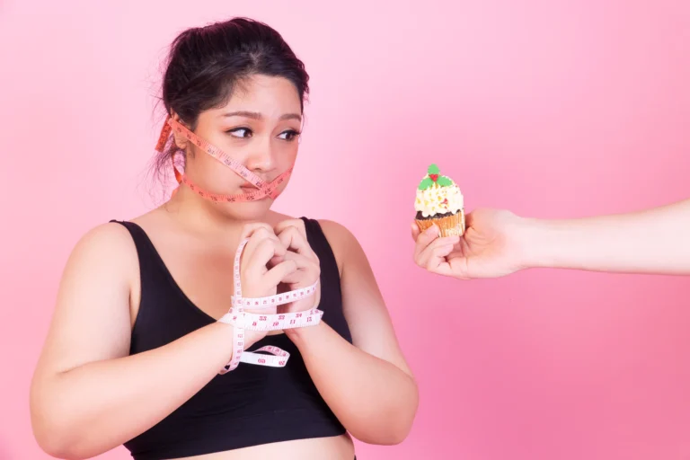Woman with her mouth taped shut and hands bound in a measuring tape refusing a cupcake, illustrating a common anti-inflammatory diet myth that healthy eating means total restriction