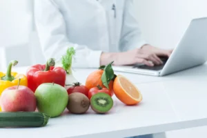 Dietitian for anti-inflammatory diet planning a meal plan on a laptop beside colourful fresh fruit and vegetables