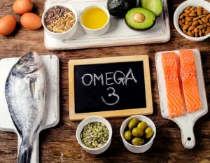 Omega-3 rich foods for anti-inflammatory nutrition, including salmon, whole fish, avocado, almonds, olives, pumpkin seeds, lentils and eggs on a wooden table