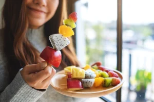 Woman holding a colourful fresh fruit skewer and a wooden plate of fruit, an easy anti-inflammatory snack idea on the Central Coast
