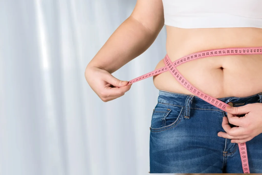 Woman measuring her waist with a pink tape measure while following a Mediterranean diet for weight management