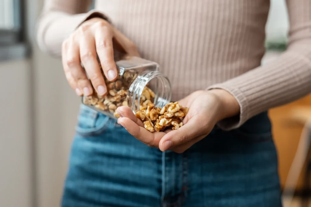 Woman pouring walnuts from a glass jar into her hand, a simple anti-inflammatory snack idea on the Central Coast