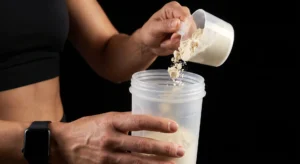 Woman scooping protein powder into a shaker bottle, one of the evidence-based supplements worth considering