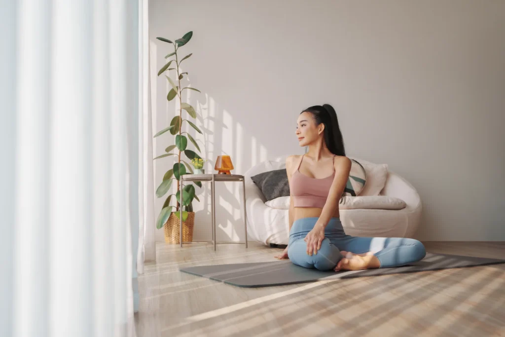 Woman doing a gentle seated stretch on a yoga mat at home, staying mobile to help limit muscle loss during immobilisation